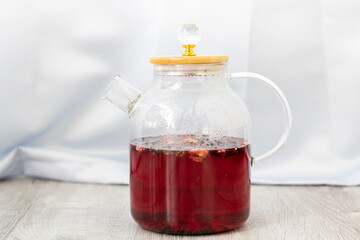 A glass teapot with red liquid is on a wooden table