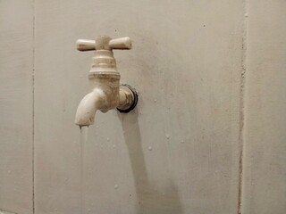 A detailed view of an old water faucet slightly open, letting a small stream drip