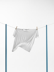 A plain white t-shirt hanging on a clothesline between two blue poles, held by wooden clothespins, against a stark white background with ample negative space
