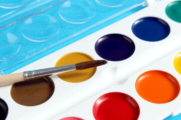 On a blue background lies a palette of watercolor paints with a brush.