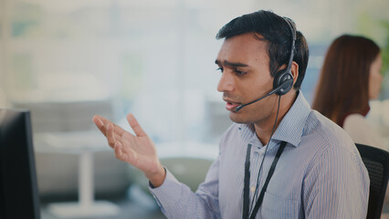 Focused male agent provides helpful tech support and excellent customer service from modern call center. He shows concern on call while assisting client with technical issue