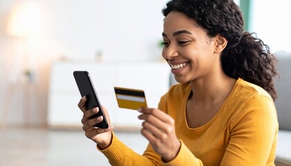 Fototapeta premium Smiling young African American woman sitting comfortably on floor at home, using smartphone and holding credit card. Relaxed mood, secure mobile banking, modern e-commerce lifestyle