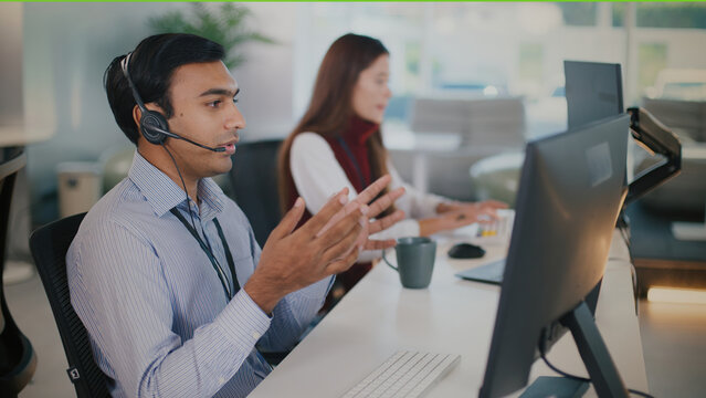 Focused male agent providing tech support and customer service at busy call center. man in headset makes call helping client in modern professional office