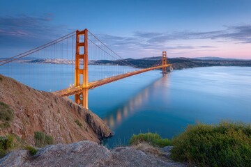 Fototapeta premium Golden Gate Bridge spans water viewed from rocky shore under a blue pink sky