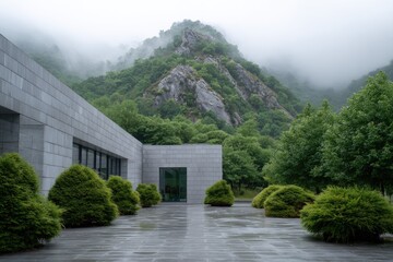 Modern building with a stone plaza set against a backdrop of misty mountains and lush greenery