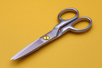 Silver scissors with a golden screw resting on a solid yellow background