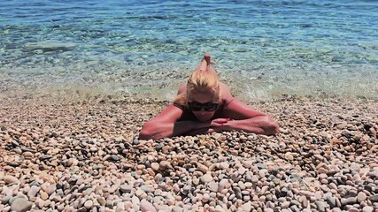 Naturist women relaxes by the sea as gentle waves wash over the shoreline under the warm Mediterranean sun, peaceful summer scene at FKK Beach Camping Skrila, Krk Island, Croatia.
