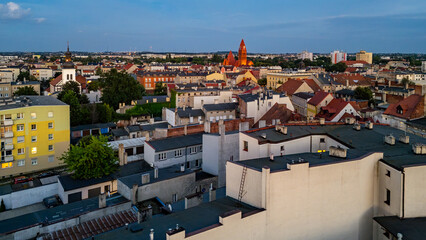 Aerial view of Ostrów Wielkopolski with rooftops of tenement buildings and the distinctive red church in the background on a clear day.