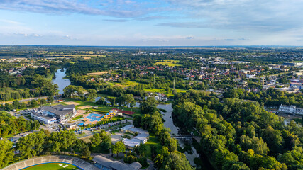 Fototapeta premium Drone photo of Kalisz showing the winding Prosna River and modern aquapark facilities surrounded by trees and urban landscape. A mix of nature and recreation in the city.