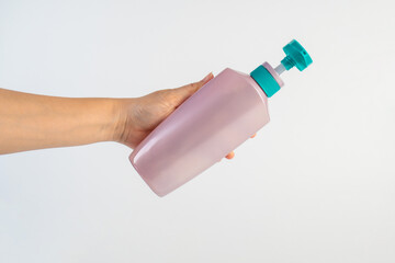 Big purple shampoo bottle in hand on white background