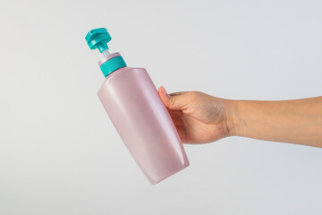 Big purple shampoo bottle in hand on white background