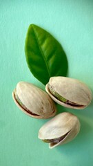 Three pistachios with a green leaf on a light green background