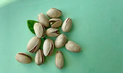 A pile of pistachios in shells and a green leaf on a light green background
