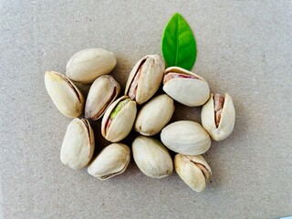 Scattered open pistachios with fresh green leaf on natural beige background, top view of healthy organic snack