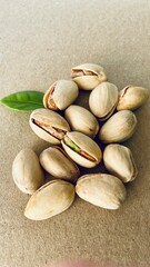 A pile of pistachios in shells and a green leaf on a gray paper background