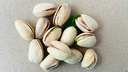 A pile of pistachios in shells and a green leaf on a gray paper background