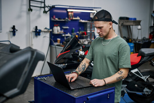 Mechanic using laptop in motorcycle workshop with tools and equipment