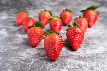 Fresh strawberries with green leaves arranged on a gray stone surface.