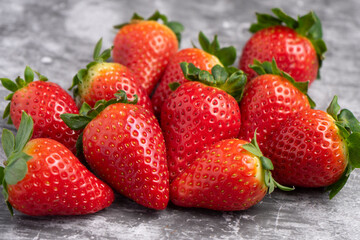 Fresh strawberries with green leaves arranged on a gray stone surface.