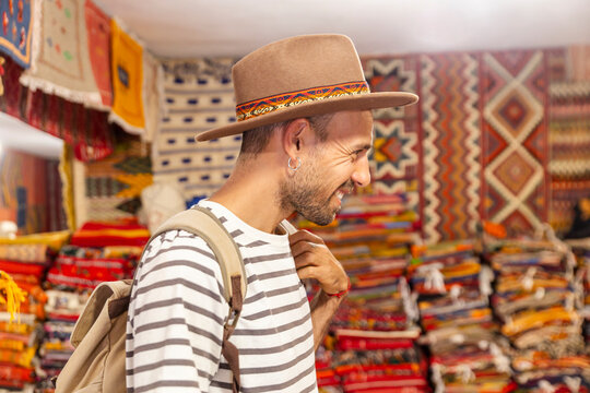 Smiling traveler in striped shirt admiring moroccan textiles at market