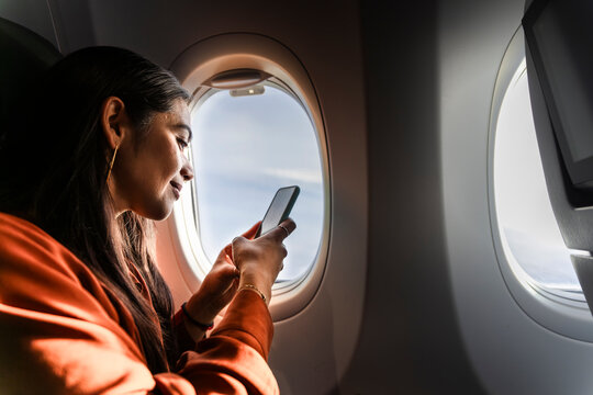 Passenger using smartphone in airplane window seat during flight