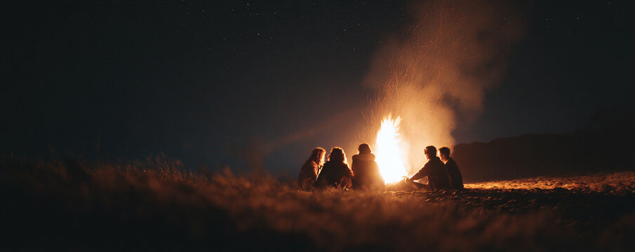 Group of friends gathered around a blazing campfire under a starry night sky, sharing stories and warmth. Represents friendship, adventure, and connection.