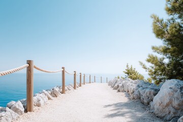 Fototapeta premium Scenic pathway along the coastline with wooden railing and rocky edges, leading to tranquil blue waters and clear sky, inviting peaceful exploration