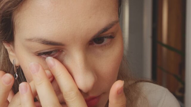 Young happy woman closeup puts on clear astigmatic lenses for vision on brown eyes. Adult girl wear lenses looking at camera, mirror reflection good eyesight, close-up smiling lips face, home room