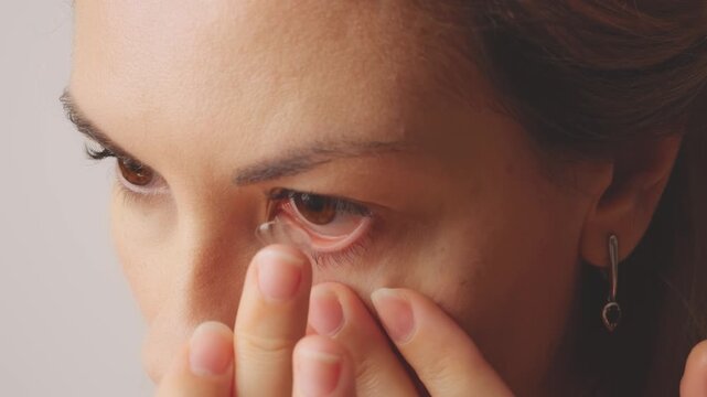 Young happy woman closeup puts on clear astigmatic lenses for vision on brown eyes. Adult girl wear lenses looking at camera, mirror reflection good eyesight, close-up smiling lips face, home room