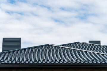 A residential roof features textured tiles under a vast, cloudy sky in a suburban area, showcasing architectural design elements