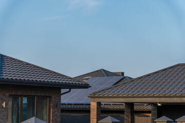 Rooftops of modern homes feature solar panels with clear blue skies above, depicting sustainable energy in an urban neighborhood