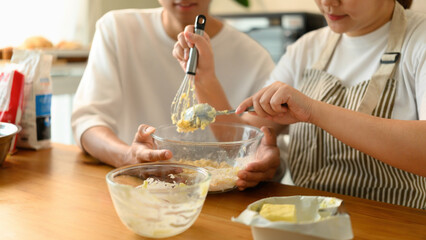 Close-up of two people mixing butter and flour in a glass bowl for cookie dough preparation in a...