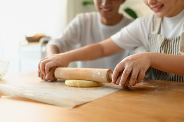 Close-up of hands rolling dough together using a wooden rolling pin during a home baking session