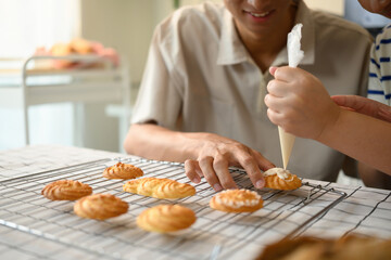 Close-up of a woman's hand adding frosting to a cookie while a man assists beside, perfect for baking and lifestyle concepts