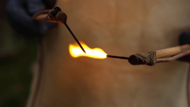 Close-up of an artisan lighting a flame between two handmade tools, capturing the precise moment of ignition during a traditional crafting or pyrography process
