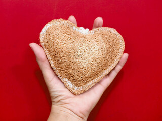 Luffa heart shape in hand,texture is coarse and fibrous.in front of red background