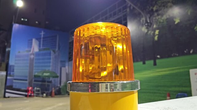 Flashing amber warning beacon light mounted on surface in indoor environment with blurred urban mural background and night lighting atmosphere for safety and alert signaling
