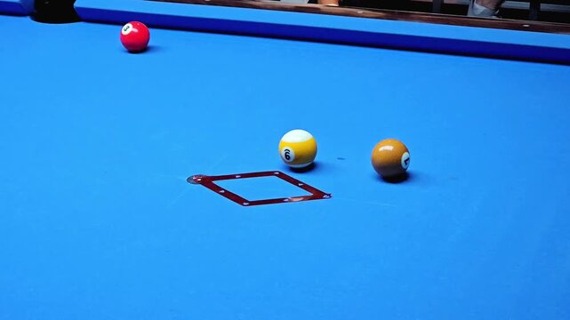 Billiard balls scattered on blue pool table with number six in focus and red marker on felt surface, gameplay situation with separated balls after break, indoor cue sport close up view