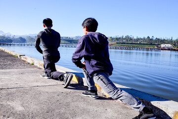 Rare View Of Two Men Stretch In A Deep Lunge Beside A Tranquil Lake, Preparing For Outdoor Exercise