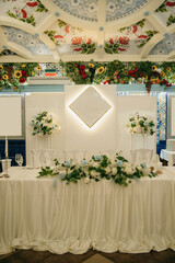 The presidium for the newlyweds in the decorated banquet hall is prepared for the celebration, white tablecloths, a set table, white flowers