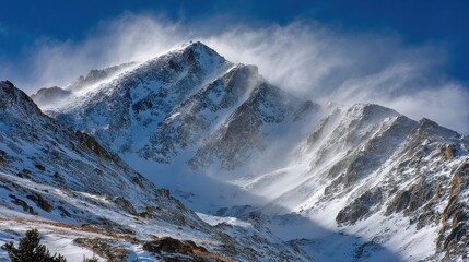 Snowy mountain peak under blue sky, wind sweeping snow