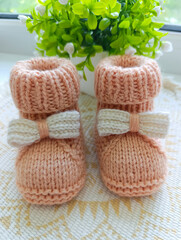 Close-up photo of beige knitted boots, on the background of a pot of flowers .Booties for a newborn