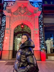 Naklejka premium Smiling woman in front of Christmas-lit building at night