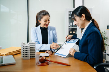 Two professional women reviewing a real estate contract with gavel, building model, and paperwork. Business law, legal advice