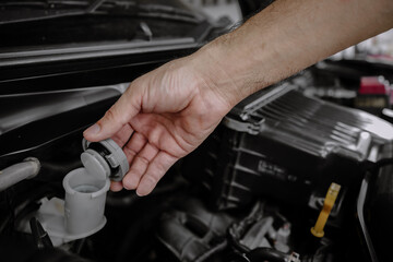 A man's hand is opening the brake fluid tank to check the level for car repair and maintenance.