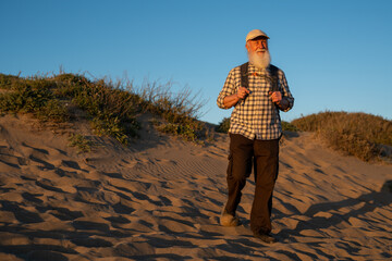 Elderly Man with a Long White Beard Hiking on Sand Dunes at Sunset