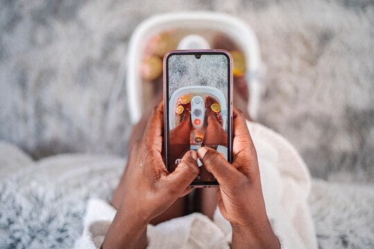 Woman taking photo of feet in foot bath with smartphone