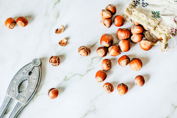 Linen pouch spilling organic hazelnuts across marble beside ornate nutcracker, clean daylight, sustainable bulk-food concept with ample negative space