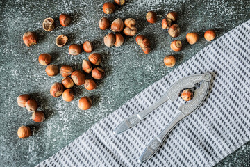 Top view of metal nutcracker, scattered filberts and fringed kitchen towel on gritty dark surface, rustic Nordic styling, perfect banner for healthy snacking ads