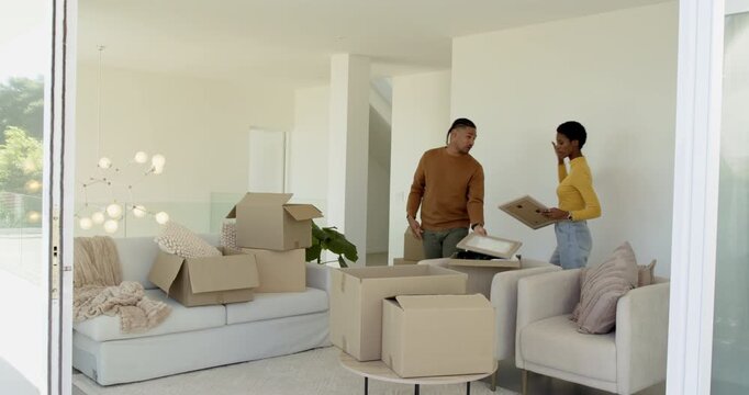 Diverse couple decorating living room, testing frames on wall, hugging before pointing sliding door